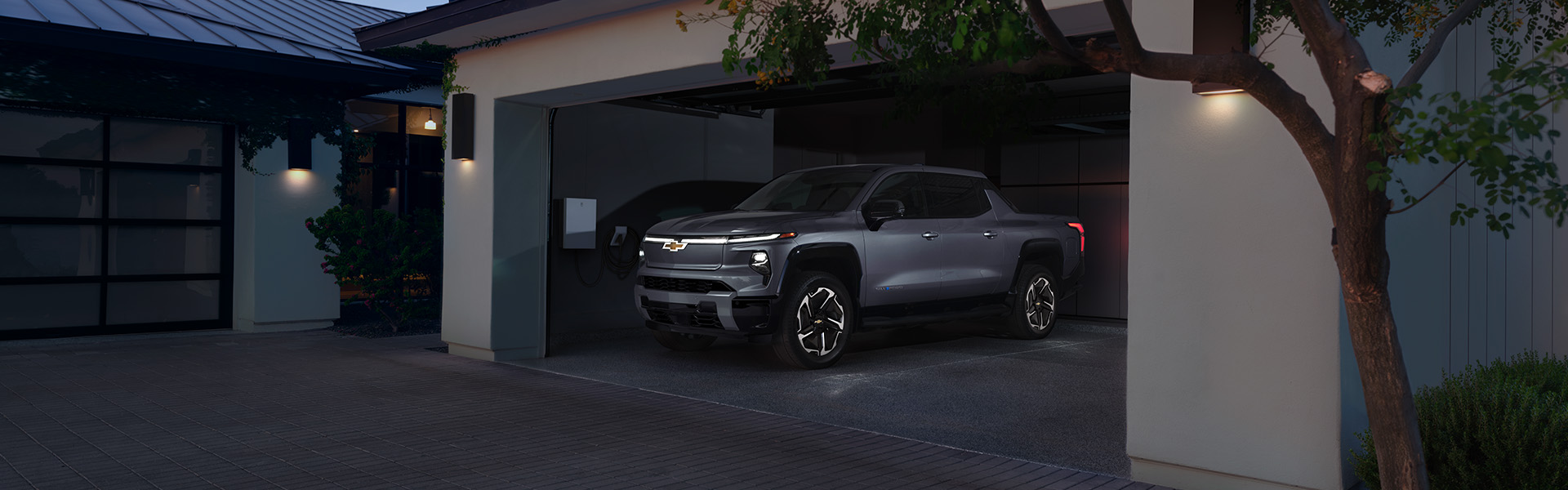 A grey 2026 Chevrolet Silverado EV parked in a modern garage, charging at night.
